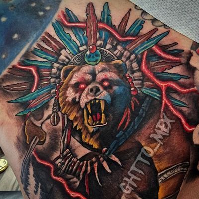 Color tattoo of a roaring bear wearing an Aztec feathered headdress with red lightning behind it.