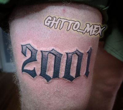 Fresh blackletter tattoo reading 2001 on the upper arm in solid black