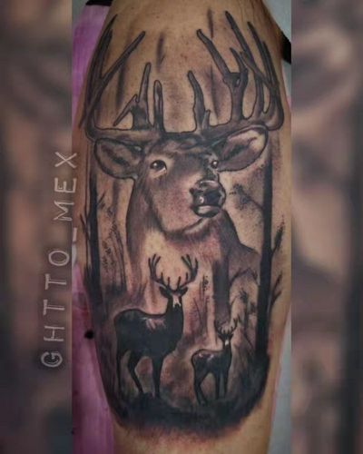 Black and grey upper arm tattoo of a buck with large antlers, a doe and a fawn in woods.