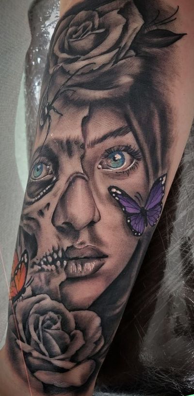 Black and grey forearm tattoo of a woman with half skull face, roses and colored butterflies