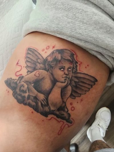 Black and grey cherub tattoo with red accents resting on clouds across a thigh