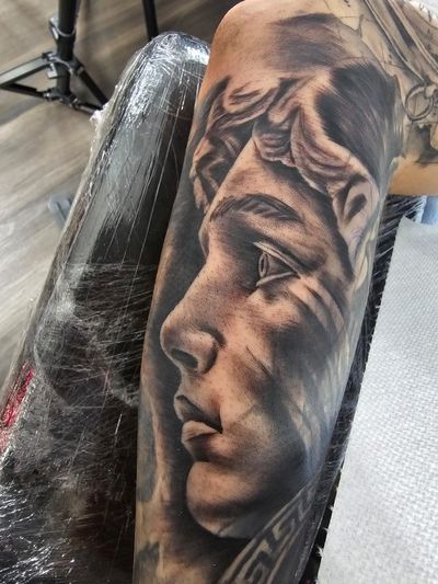 Black and grey realism portrait of a classical statue woman with a leafy crown on a forearm