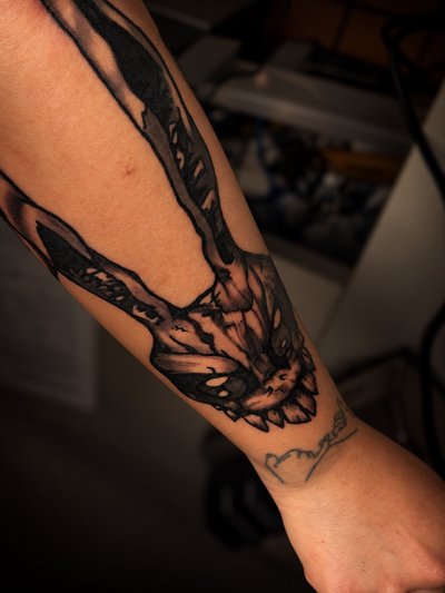 Black and grey illustrated rabbit face with long ears and exposed teeth on the forearm