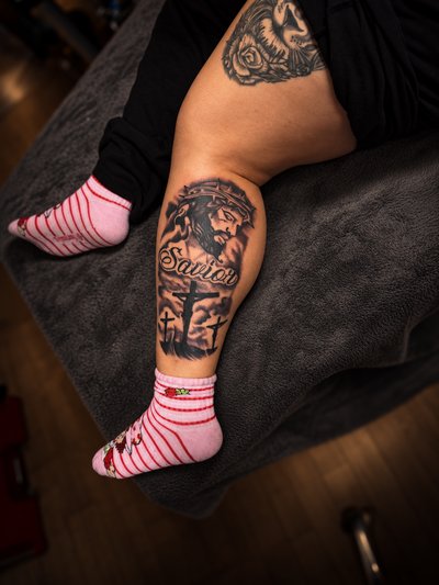Black and grey portrait of Jesus with a crown of thorns, Savior script and three crosses on the calf