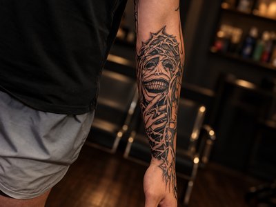 Black and grey skeletal face with a thorned crown and elongated fingers along the forearm