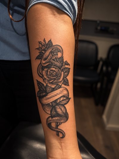 Black and grey snake winding around roses and leaves on the upper arm
