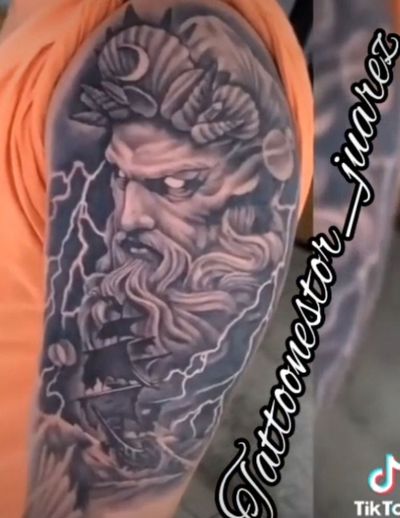 Black and grey upper arm tattoo of a bearded Greek god with lightning bolts, storm clouds and a sailing ship