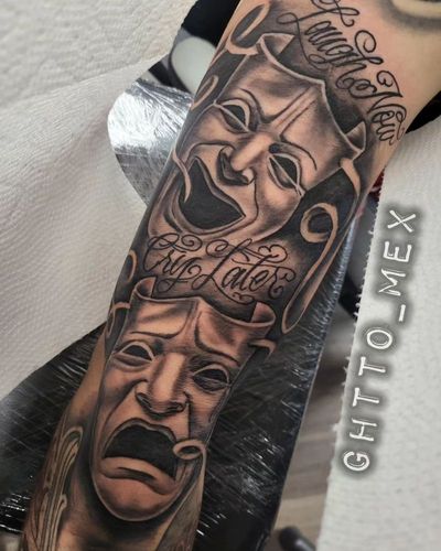 Black and grey forearm piece with laugh now cry later theater masks and flowing script lettering.