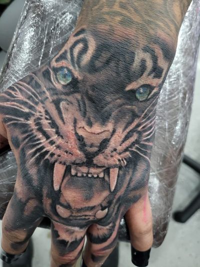 Fresh black and grey tiger face covering the back of the hand, with green eyes, seen through plastic wrap.