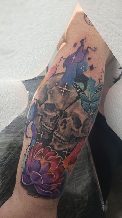 Two stacked skulls in gray wash with watercolor splashes, a blue butterfly and a purple lotus.