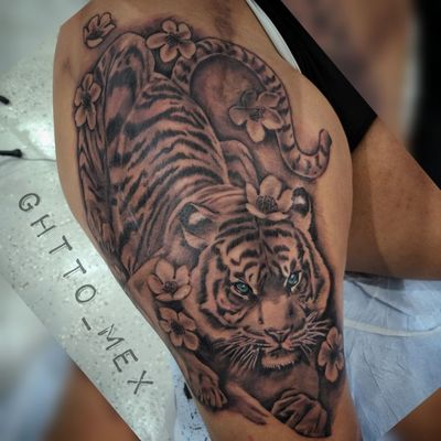 Black and grey tiger with bright blue eyes and blossoms wrapping the thigh