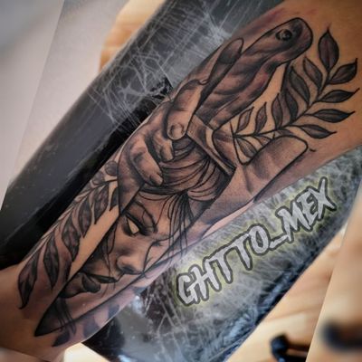 Black and grey forearm tattoo of a woman's face beneath a hand and olive branch leaves
